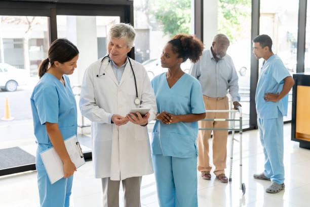 istock Cheerful senior doctor talking to diverse nurses while while holding a tablet at the hospital entrance 1596312642