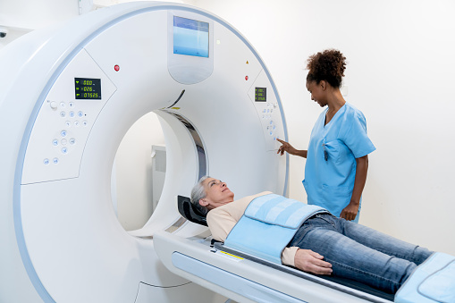 Female black technician adjusting the machine before starting the CAT scan on mature female patient - Healthcare concepts
