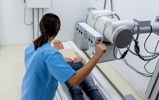 Female radiologist adjusting the machine while explaining the procedure to patient lying down - Healthcare concepts