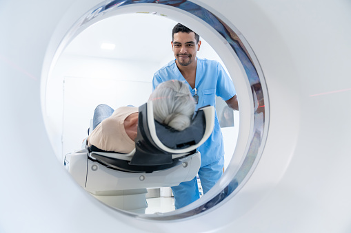 Cheerful male technician adjusting the machine before starting the CAT scan of an unrecognizable senior woman lying down on machine  - Healthcare concepts