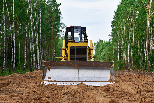 Dozer on forest clearing for road construction. Yellow Bulldozer at forestry work Earth-moving equipment at road work, land clearing, grading, pool excavation, utility trenching.