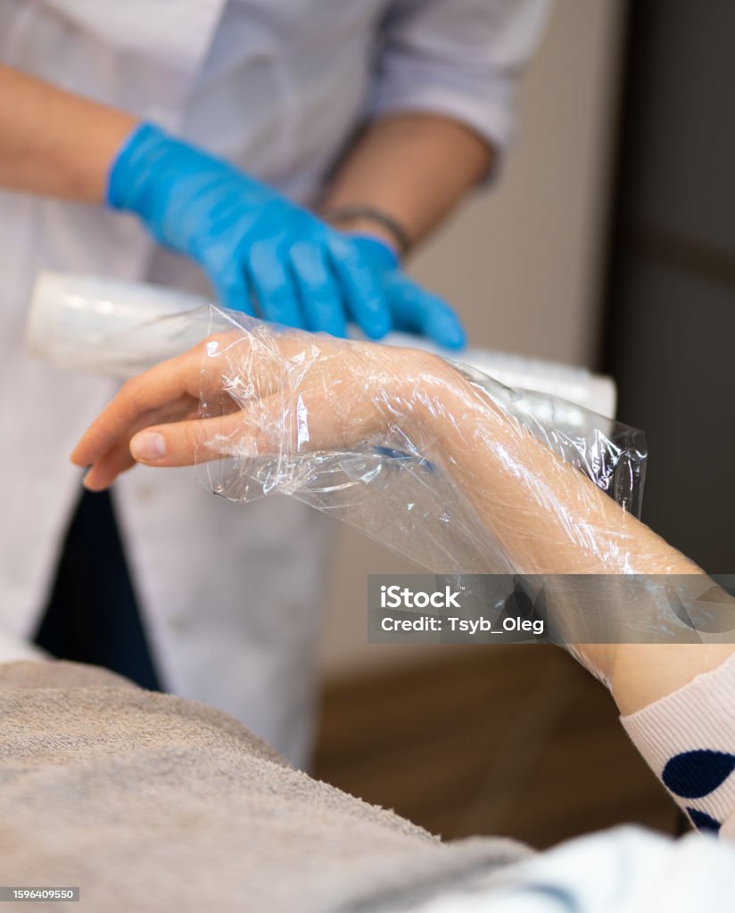 close-up masseur makes a hand massage in a beauty salon wrapping with film and cellophane Adult Stock Photo