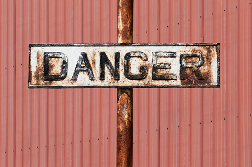 Danger sign in white with black text and red background. Sign is old, weathered and aged.