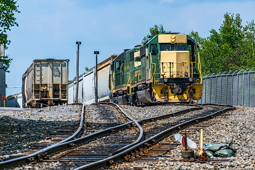 Industrial rail infrastructure: not pretty but vital to economic efficiency.  Low angle view two diesel locomotives shunting (drilling, placing) railroad cars for customer in new industrial estate. Rail infrastructure established to facilitate rail transportation in Hazleton, Pennsylvania.  In the foreground the direction marker indicates the hand-operated points (switch, turn-out) are set for the train. Logos and ID edited.