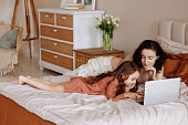 Mother and daughter using laptop on bed in holiday at home.