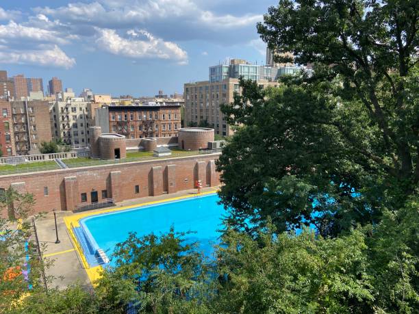 Hillside view of the historic outdoor pool and recreation center in Jackie Robinson Park on a hot summer day in Harlem, New York City View of the historic outdoor public pool in Jackie Robinson Park and the green roof at the Jackie Robinson Recreation Center from the top of a tree-lined hill on a sunny summer day in Harlem, New York City harlem park stock pictures, royalty-free photos & images