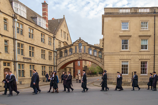 Oxford, United Kingdom - November 12th 2022: A line of students on their way to their graduation ceremony pass Hertford Bridge, more commonly known as the Bridge of Sighs after its resemblance to the bridge of the same name in Venice.