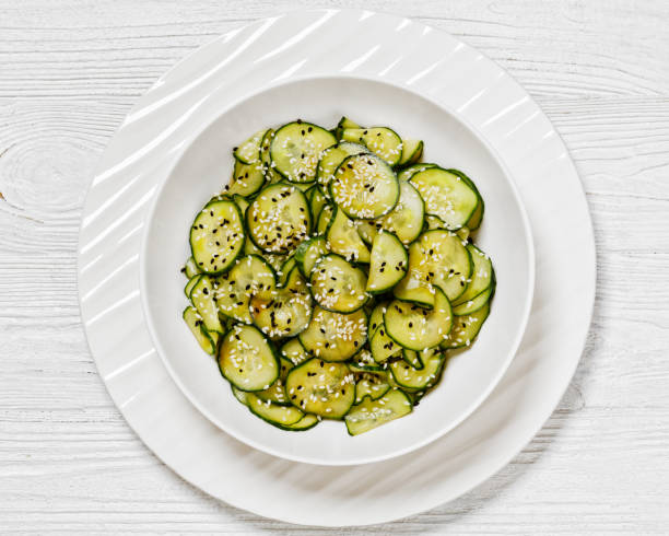 Sunomono, Japanese Cucumber Salad in a white bowl Sunomono, Japanese Cucumber Salad, sliced cucumbers with Asian dressing of soy sauce, rice vinegar, sesame oil and sugar in white bowl on white wooden table, flat lay, close-up sunomono stock pictures, royalty-free photos & images