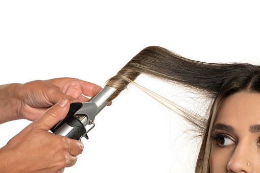 Stylist using curling iron for hair curls, close-up, isolated on white studio background