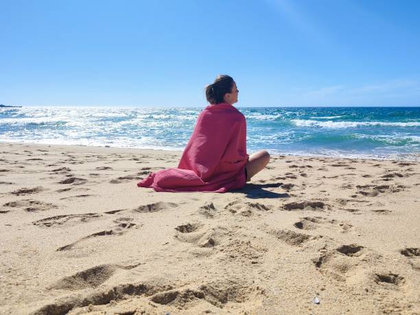 istock Woman sitting on the sand looking at the ocean 1596648395