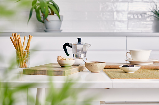 Morning coffee art serving, on a white kitchen table in a modern white kitchen filled with plants, image  with a free space for copy