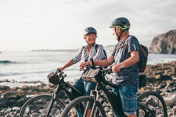 heureux couple de personnes âgées sportives avec leurs vélos à la plage. personnes âgées exprimant satisfaction et liberté en vacances ou à la retraite - senior couple cycling beach bicycle photos et images de collection