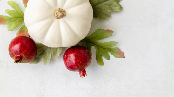 A white pumpkin, pomegranate picks, and fabric leaves on a textured white background