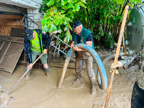 Nozice, Slovenia - August 5, 2023: Man removing river silt residue with water pump with hose after flooding of Kamniska Bistrica river at Nozice village.