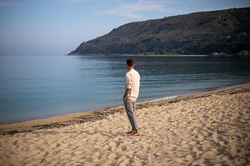 A young man in a relaxed pose on a sandy beach, with a tranquil ocean in the background
