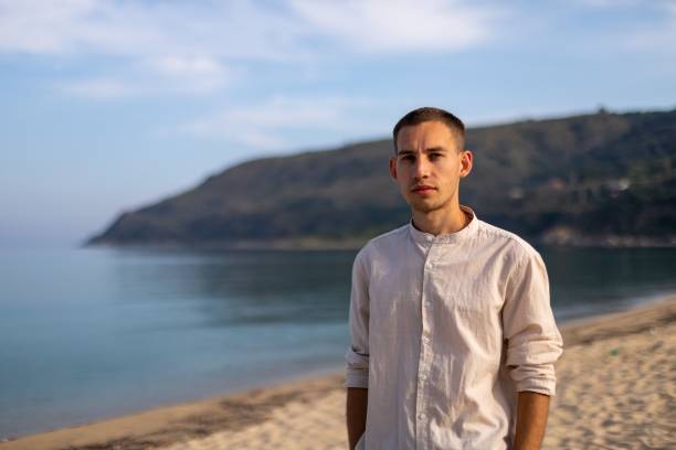 istock Young man in a relaxed pose on a sandy beach, with a tranquil ocean in the background 1596820803