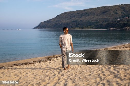 istock Young man in a relaxed pose on a sandy beach, with a tranquil ocean in the background 1596820806