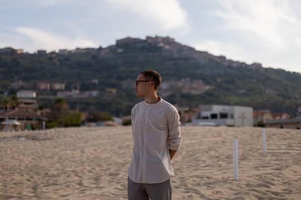 istock Young man in a relaxed pose on a sandy beach, with a tranquil ocean in the background 1596820808