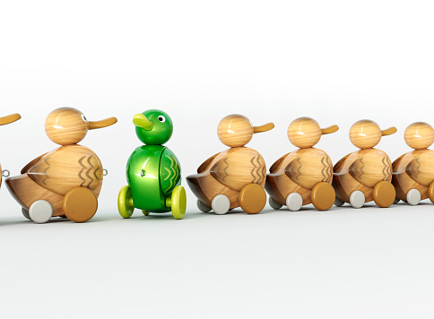 A non-conformist depiction of a green shiny toy duck in an opposite direction to a row of ordinary wooden ducks on an isolated background - 3D render