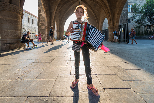 Refugee Syrian little girl on the island of Rhodes earns her money by playing accordion to tourists on the street. August 5, 2016
