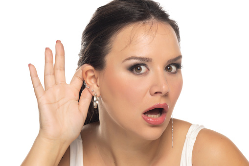 Young brunette woman wearing casual white shirt with hand over ear listening and hearing to rumor or gossip on a white studio background