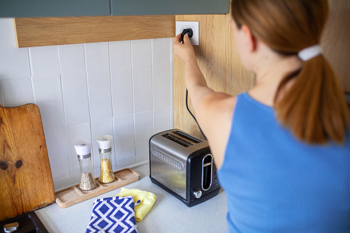 Woman using toaster to make breakfast in kitchen at home