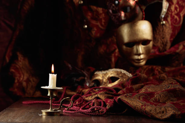 istock Burning candle in an old brass candlestick and carnival masks. 1596941545