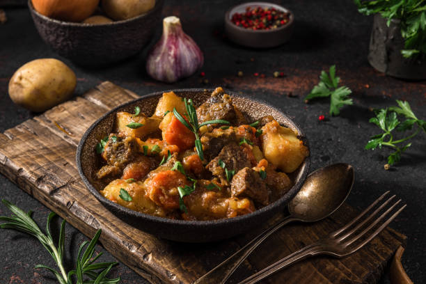 guiso irlandés hecho con carne de res, patatas, zanahorias y hierbas en un plato con cubiertos sobre fondo negro - carrot close up silverware cutting board fotografías e imágenes de stock