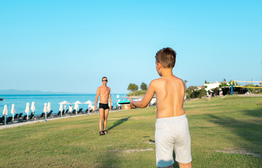 Father and son playing frisbee in the park near the coastline.