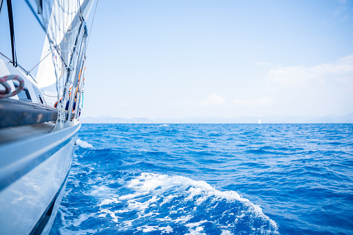 Yacht sailing in an open sea. Close-up view of side of the boat. Clear sky after the rain, waves and water splashes. High quality photo