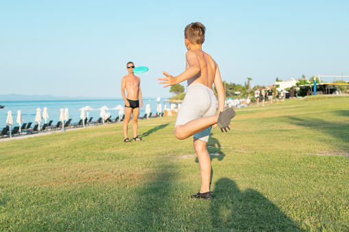 Father and son playing frisbee in the park near the coastline.