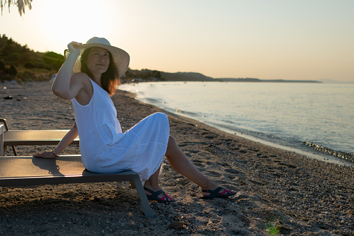 Woman with straw hat is enjoying herself on the beach in the sunset.