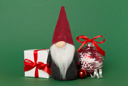 A Christmas gnome with trees and lights behind it and light on a red background.