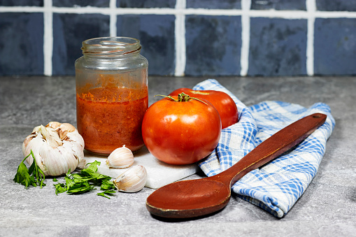 tomato sauce in glass bottle with parsley and garlic on cutting board with wooden spoon on grunge gray floor