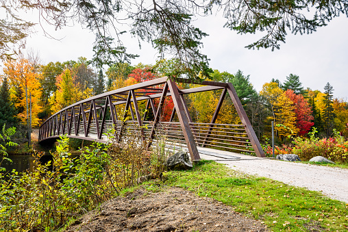Steel suspension bridge for pedestrians and cyclists over a river on a cloudy autumn day. Stunning autumn colours in background. Bancroft, ON, Canada.