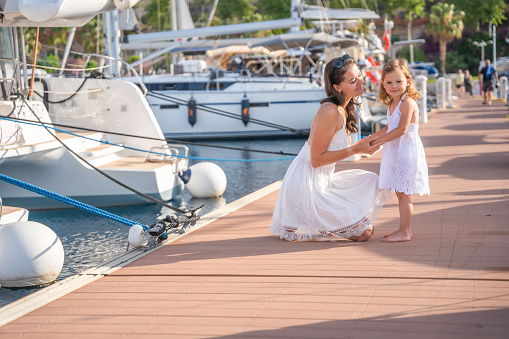 Happy mother and daughter child having fun on luxury yachts on background in marina. Family travel, lifestyle, vacation concept. High quality photo