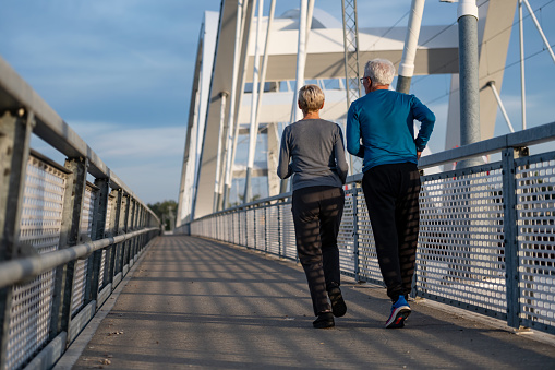 Cheerful active senior couple jogging together outdoors on the bridge. Healthy activities for elderly people.