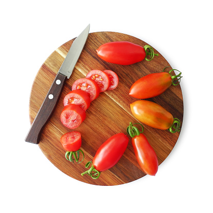 Fresh ripe organic red tomatoes whole and sliced on round wooden cutting board with knife isolated on white background top view