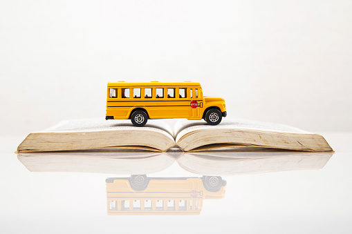 Yellow retro school bus on book on white background