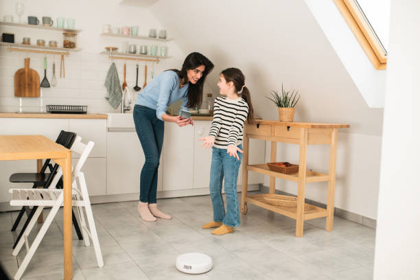istock Girl using smartphone and helping her mom to adjust smart vacuum cleaner 1597360837