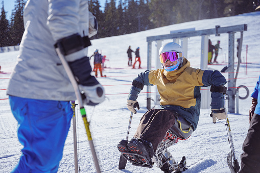 An adaptive athlete who is using a sit-ski smiles while talking with a friend while on a weekend winter ski trip in the Pacific Northwest region of the United States.