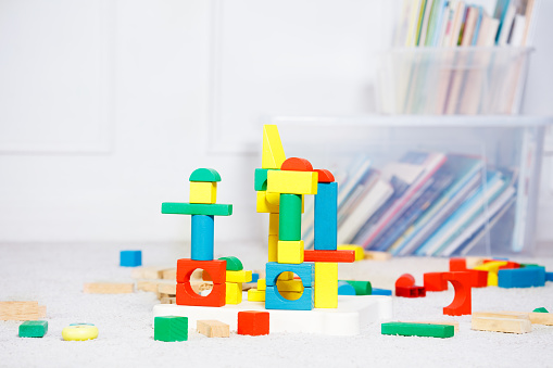 Group of toy wooden color blocks, towers build of them over boxes of toys and books around