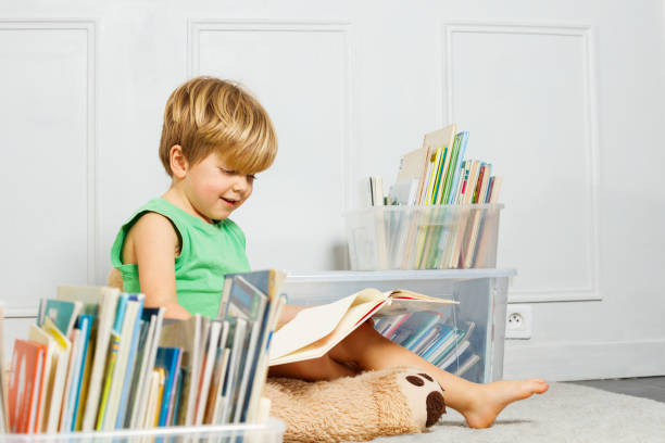 portrait of a boy reading on white carpet, books in boxes around - child prodigy imagens e fotografias de stock