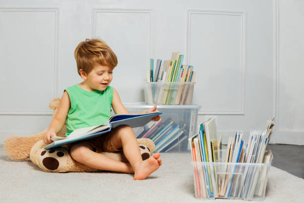 child read a text while being surrounded by many books in boxes - child prodigy imagens e fotografias de stock