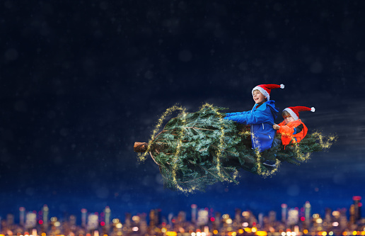 Magical image of two boys fly on the Christmas tree over city at night wearing Santa hat holding together