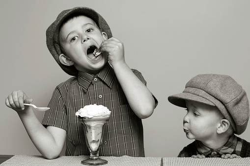 A photograph of a little boy yearning for the sundae that his brother is eating.  This photograph was converted to black and white with additional toning added to give it a vintage feel.