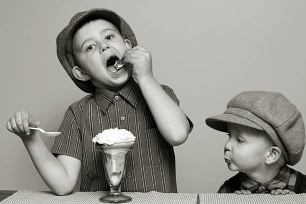 Brothers With A Sundae A photograph of a little boy yearning for the sundae that his brother is eating.  This photograph was converted to black and white with additional toning added to give it a vintage feel. desire photos stock pictures, royalty-free photos & images