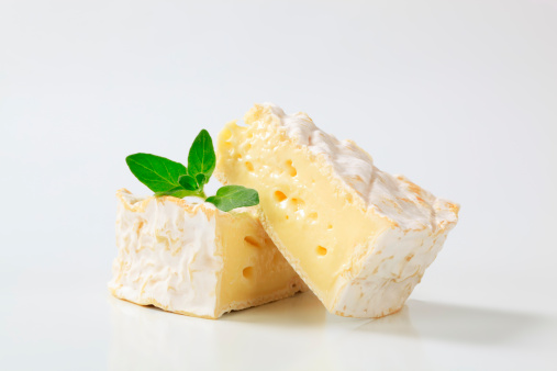 two triangular pieces of a ripe camembert cheese with green leaves of a basil
