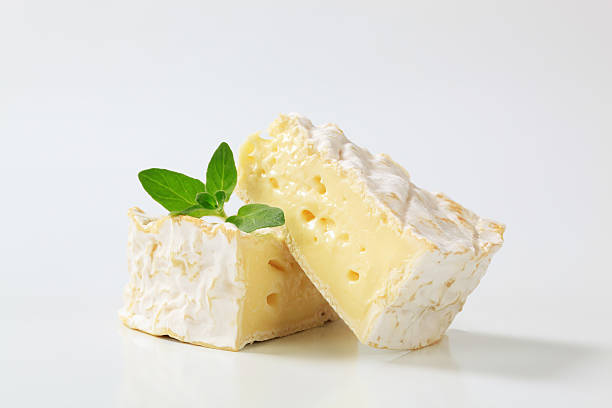 camembert cheese two triangular pieces of a ripe camembert cheese with green leaves of a basil brie stock pictures, royalty-free photos & images