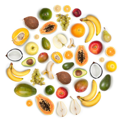 Composition made with many healthy fruits arranged together in a circular round shape on white background: apples, bananas, lemons, oranges, mangos, pears, avocado, grapefruit, coconut